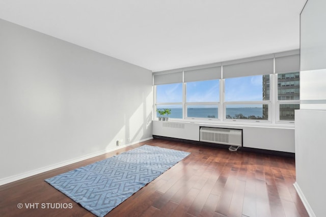 empty room featuring dark hardwood / wood-style flooring, a water view, and an AC wall unit