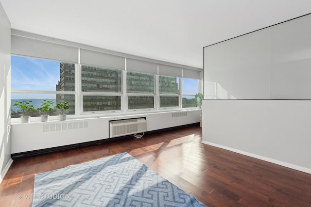 spare room with a wealth of natural light, a wall mounted air conditioner, a water view, and dark hardwood / wood-style floors