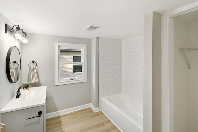 bathroom with hardwood / wood-style flooring, vanity, and tiled shower / bath