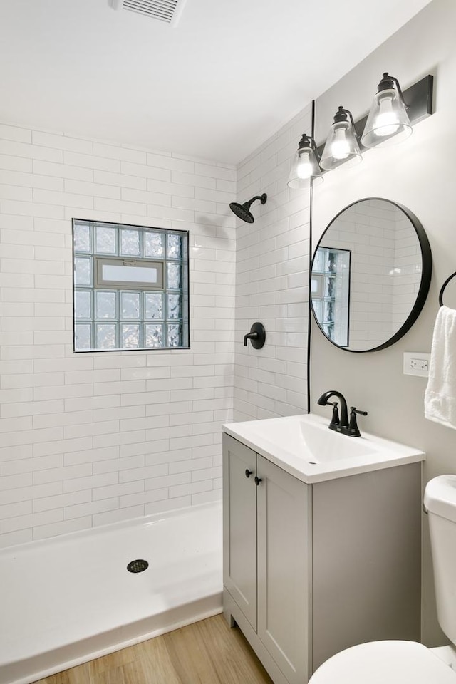 bathroom with hardwood / wood-style floors, vanity, a tile shower, and toilet