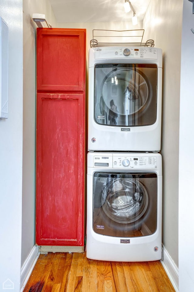 clothes washing area featuring stacked washer / dryer, cabinets, and light hardwood / wood-style floors