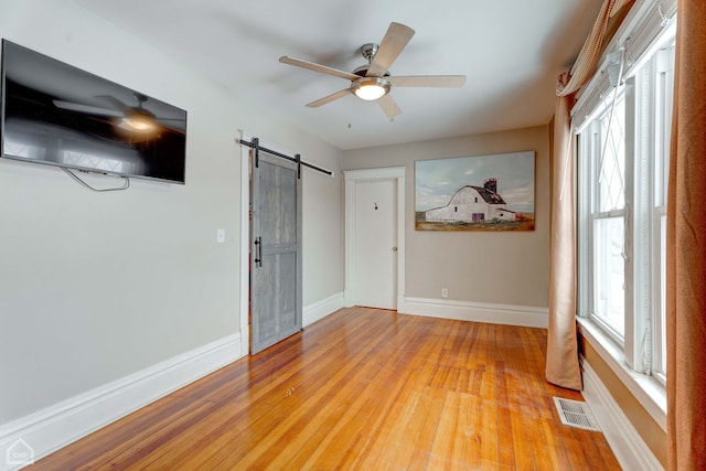 spare room featuring ceiling fan, a barn door, and light wood-type flooring