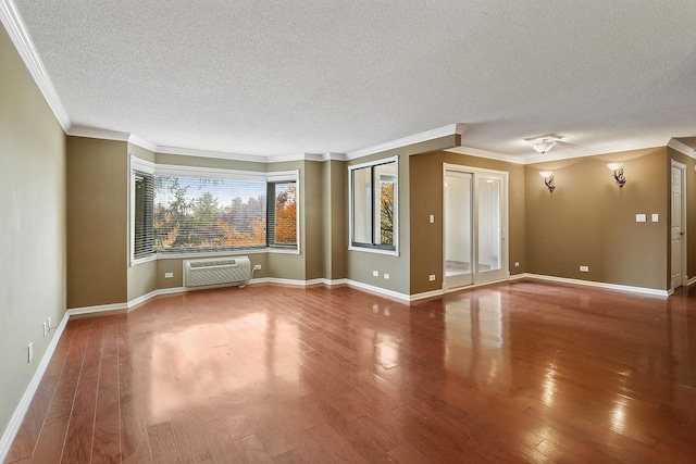 unfurnished living room with a wall mounted air conditioner, a textured ceiling, hardwood / wood-style flooring, and crown molding