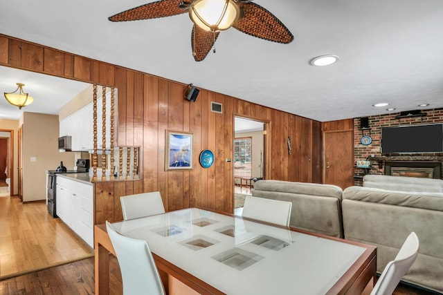 dining room featuring ceiling fan, light wood-type flooring, a fireplace, and wooden walls