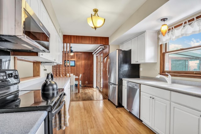 kitchen with white cabinets, hanging light fixtures, wooden walls, and stainless steel appliances