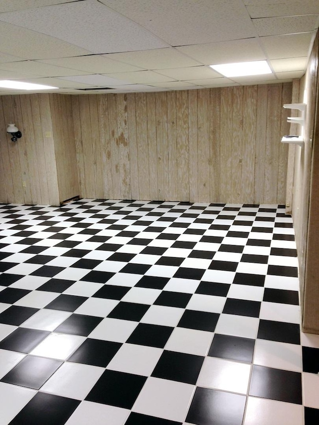 basement featuring wood walls and a drop ceiling