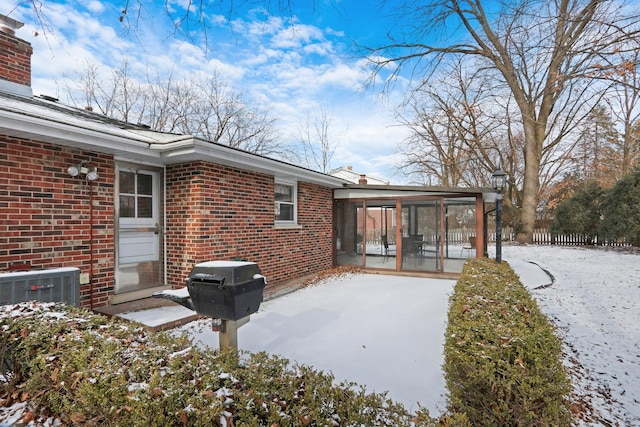 snow covered rear of property featuring a sunroom and cooling unit