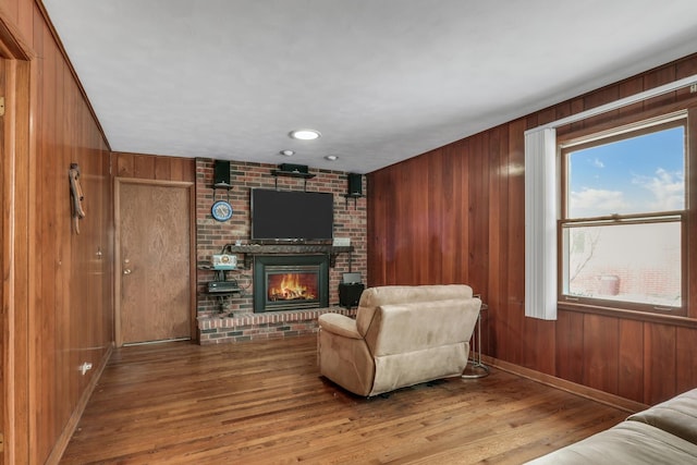 living room featuring wood-type flooring, a brick fireplace, and wood walls