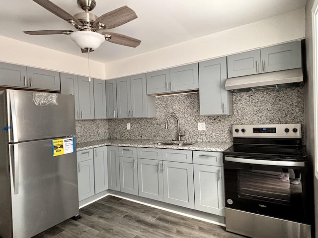 kitchen with light stone countertops, appliances with stainless steel finishes, dark hardwood / wood-style flooring, ceiling fan, and sink