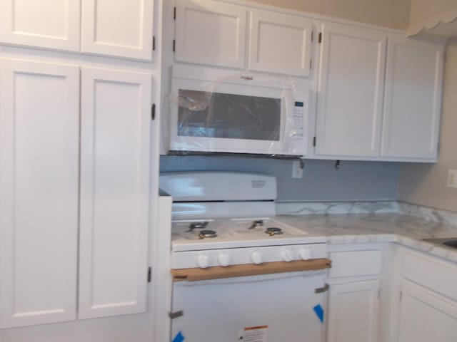 kitchen with white cabinetry, light stone countertops, and white appliances