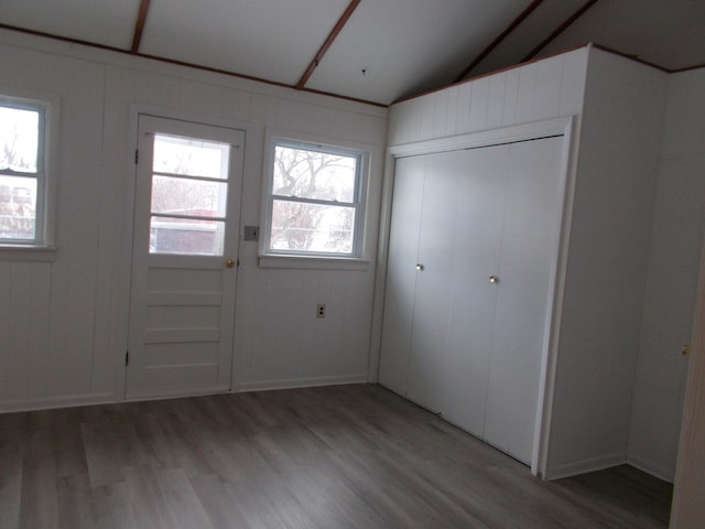 foyer featuring wood-type flooring, wooden walls, vaulted ceiling, and a healthy amount of sunlight