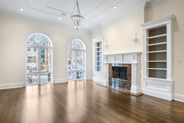 unfurnished living room featuring a high end fireplace, built in shelves, dark hardwood / wood-style flooring, and ornamental molding