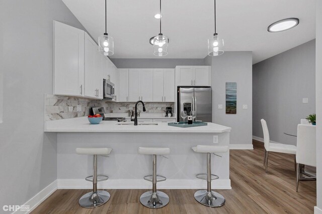 kitchen featuring kitchen peninsula, appliances with stainless steel finishes, tasteful backsplash, white cabinetry, and a breakfast bar area