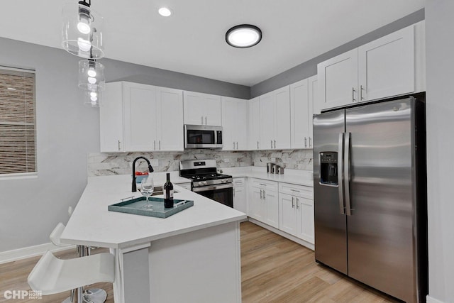 kitchen with kitchen peninsula, a kitchen bar, stainless steel appliances, white cabinets, and hanging light fixtures