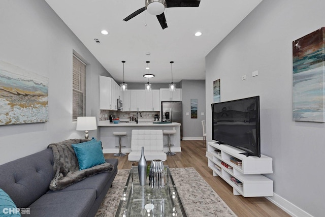 living room with light hardwood / wood-style floors, ceiling fan, and sink