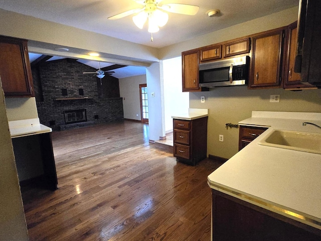 kitchen featuring dark hardwood / wood-style flooring, a brick fireplace, brick wall, ceiling fan, and sink