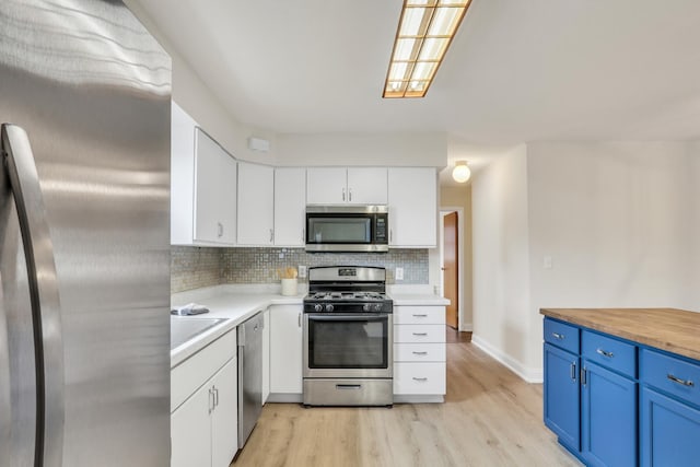 kitchen featuring white cabinets, blue cabinetry, appliances with stainless steel finishes, tasteful backsplash, and butcher block counters