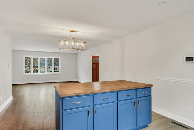 kitchen featuring butcher block counters, hanging light fixtures, blue cabinetry, a kitchen island, and wood-type flooring