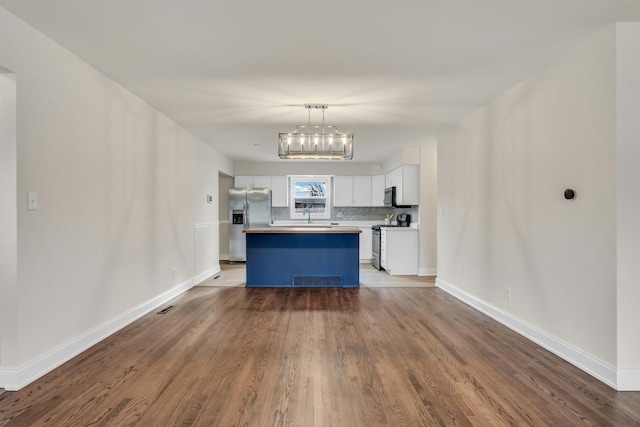 kitchen with stainless steel appliances, a kitchen island, pendant lighting, wood-type flooring, and white cabinets