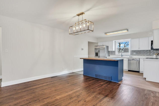 kitchen with appliances with stainless steel finishes, dark hardwood / wood-style flooring, pendant lighting, white cabinets, and a center island