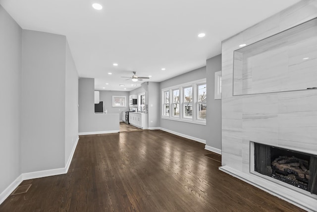 unfurnished living room with ceiling fan, a large fireplace, and dark hardwood / wood-style flooring