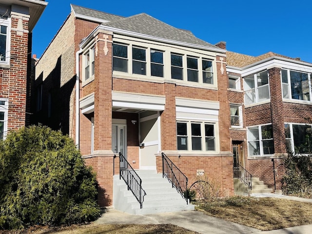 view of front facade featuring brick siding and roof with shingles