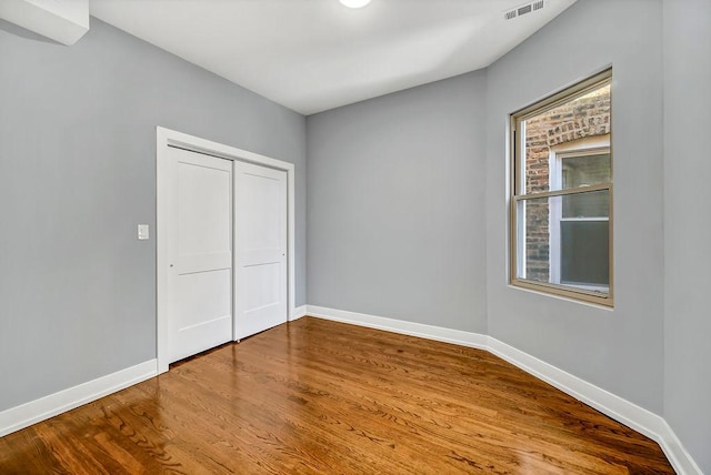 unfurnished bedroom featuring a closet, visible vents, baseboards, and wood finished floors