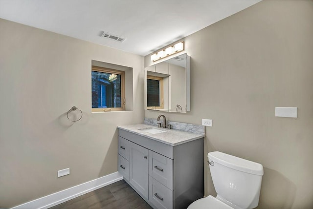 bathroom with toilet, wood finished floors, vanity, visible vents, and baseboards