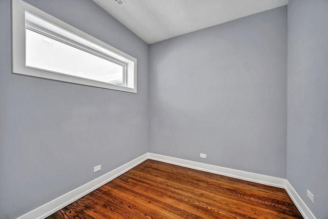 empty room with dark wood-style flooring, visible vents, and baseboards