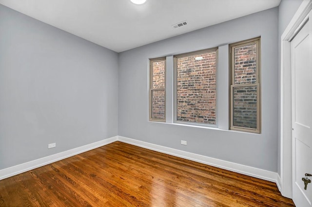 empty room with dark wood-type flooring, visible vents, and baseboards