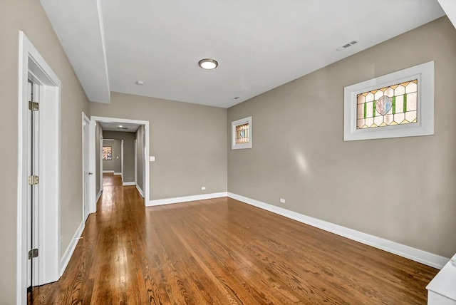 spare room with wood finished floors, visible vents, and baseboards