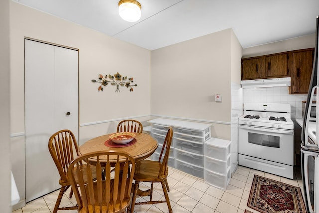 kitchen with dark brown cabinetry, white range with gas stovetop, tasteful backsplash, light tile patterned floors, and stainless steel fridge