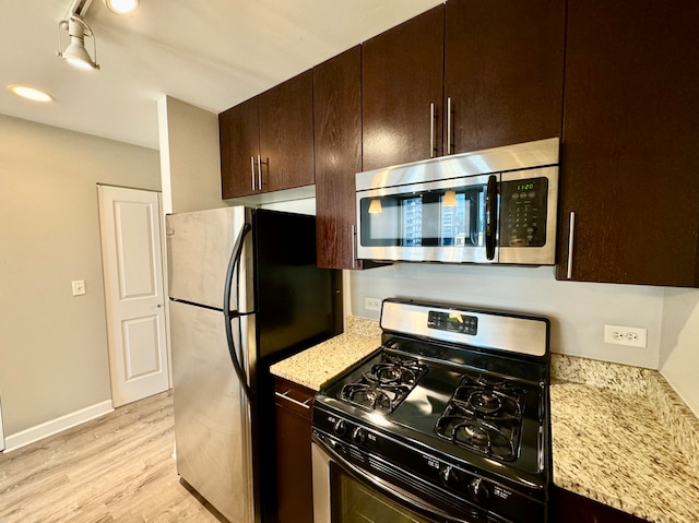 kitchen with dark brown cabinetry, rail lighting, stainless steel appliances, light stone counters, and light hardwood / wood-style floors