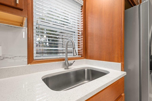 kitchen featuring light stone counters, sink, and stainless steel refrigerator