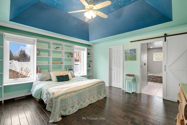 bedroom with ceiling fan, dark hardwood / wood-style floors, ensuite bathroom, vaulted ceiling, and a barn door