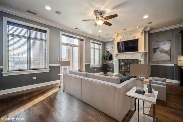 living room with dark wood-type flooring, a premium fireplace, crown molding, and ceiling fan