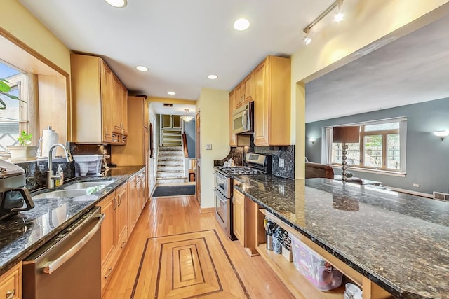 kitchen with rail lighting, dark stone counters, stainless steel appliances, sink, and light hardwood / wood-style flooring