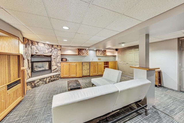 carpeted living room featuring a paneled ceiling and a stone fireplace