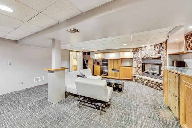 carpeted living room with a stone fireplace and a drop ceiling