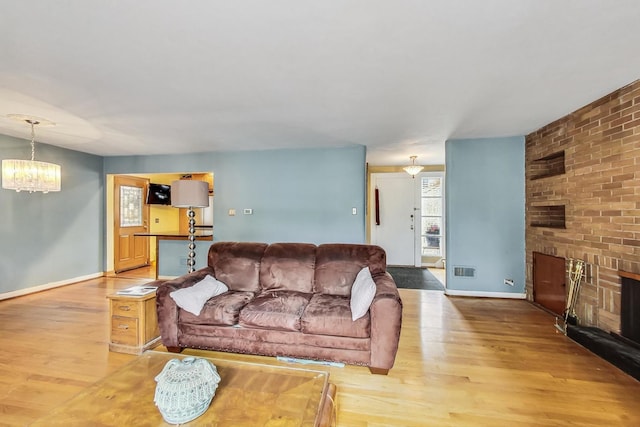 living room with light hardwood / wood-style floors, a chandelier, and a brick fireplace