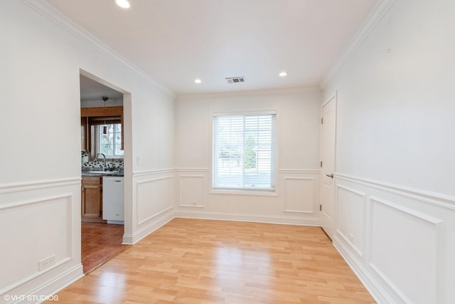 empty room featuring crown molding, light wood-type flooring, and sink