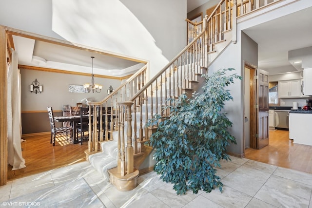 stairway with a raised ceiling, an inviting chandelier, and tile patterned flooring