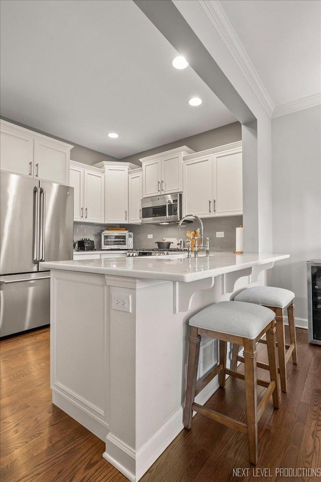 kitchen featuring appliances with stainless steel finishes, white cabinetry, backsplash, and kitchen peninsula