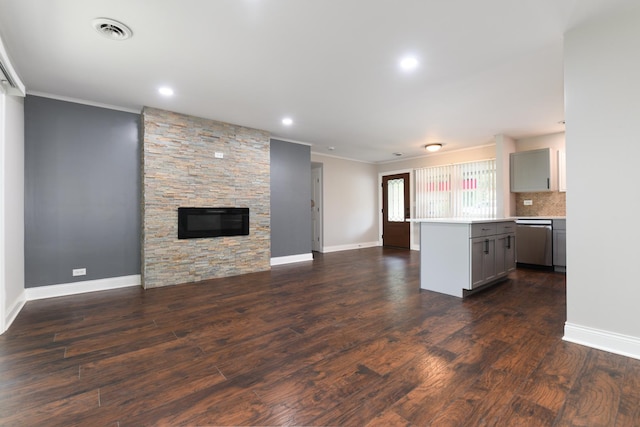 kitchen featuring stainless steel dishwasher, gray cabinetry, dark wood-type flooring, a kitchen island, and a stone fireplace