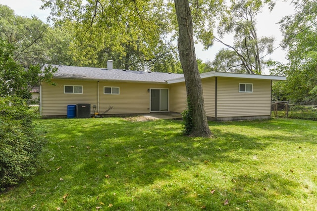 rear view of house with central air condition unit and a lawn