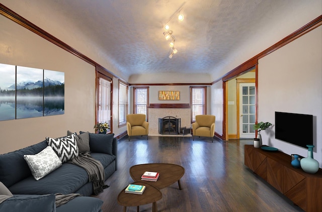 living room with rail lighting, ornamental molding, a textured ceiling, hardwood / wood-style floors, and a tiled fireplace