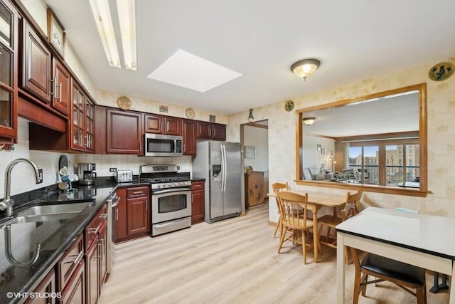 kitchen featuring decorative backsplash, appliances with stainless steel finishes, a skylight, sink, and light hardwood / wood-style floors