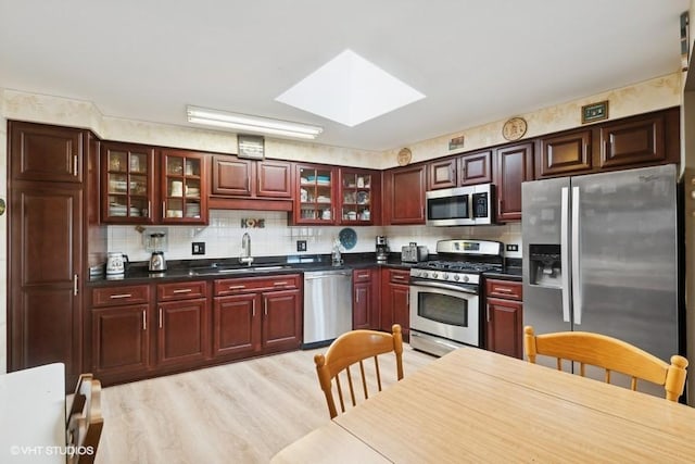 kitchen featuring decorative backsplash, appliances with stainless steel finishes, light wood-type flooring, a skylight, and sink