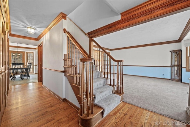 staircase featuring hardwood / wood-style floors, a notable chandelier, and crown molding