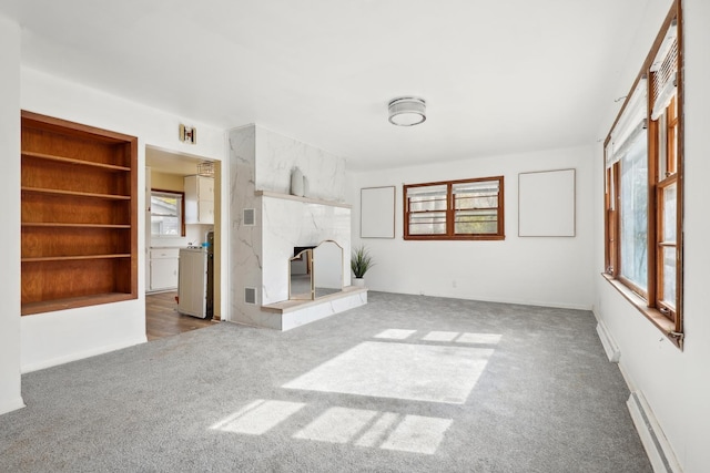 unfurnished living room featuring carpet flooring, built in shelves, baseboard heating, and a fireplace